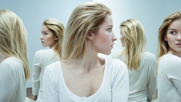Shot of a young woman dressed in white looking back with anxiety at her reflections in the mirror
