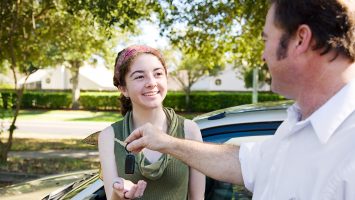 Young woman being handed the car keys by her father or driving instructor.