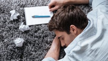 Close up portrait of an exhausted young man sleeping on a carpet with notepad