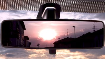 Sunset on a field, reflected in the rearviewmirror of a car