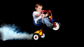 Toddler popping a wheelie on a tricycle with smoke caused by burning rubber